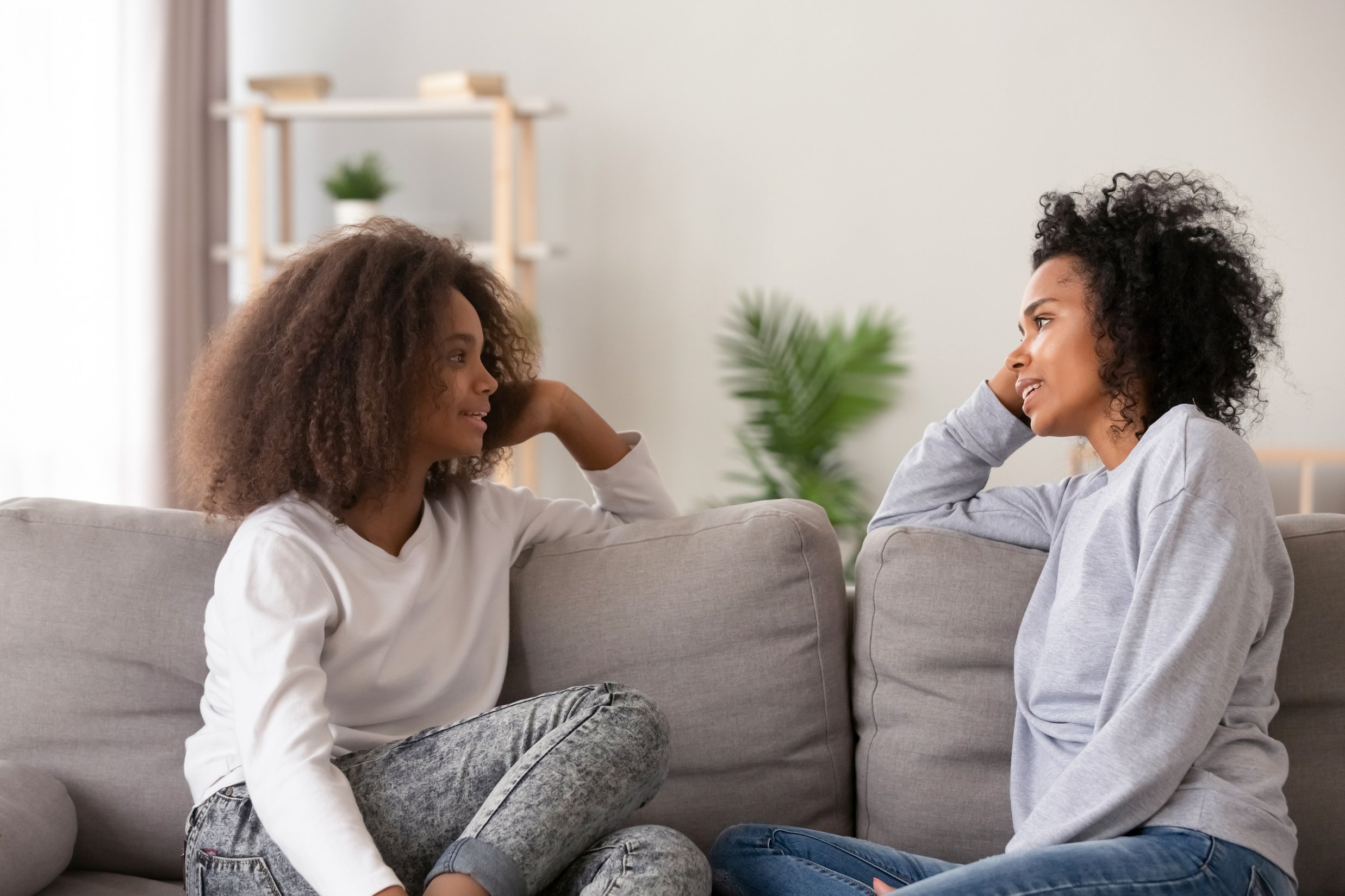 African young mom listening teen daughter sitting on couch together